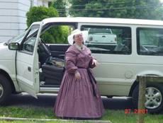 Woman in a civil war era dress stands next to a van.