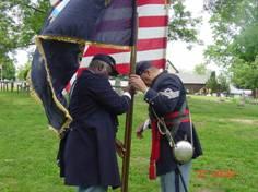 Two men in Civil War Union soldier uniforms hold flags of the United States and Pennsylvania.