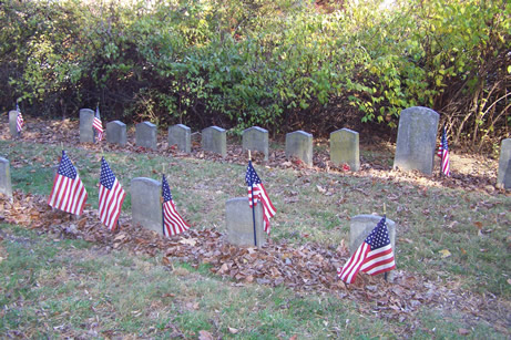 Several rows of short government issued military headstones, the front row adorned with U.S. flags and the rear row having pointed tops.